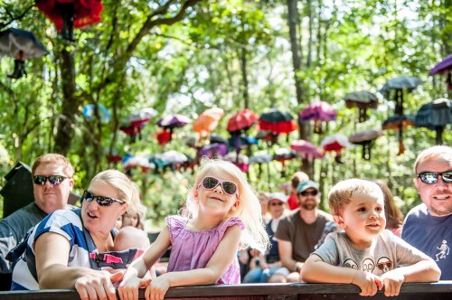A group of people, including children, enjoy a ride in a forest with colorful umbrellas hanging above them.