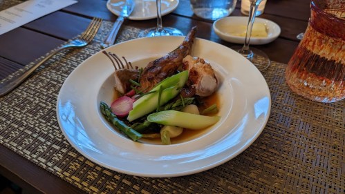 A plated dish featuring roasted meat, asparagus, and radishes, served in a savory sauce on a textured table setting.
