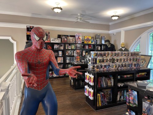 A life-sized Spider-Man figure stands in a store filled with shelves of collectibles and comic books.