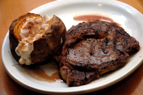 A plate featuring a juicy steak with a side of baked sweet potato topped with marshmallows.