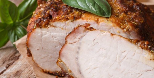 Sliced roasted meat with a crispy crust, garnished with a fresh basil leaf on a wooden surface.