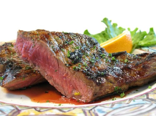 Grilled steak slices on a plate, garnished with herbs and served with a slice of orange and lettuce.