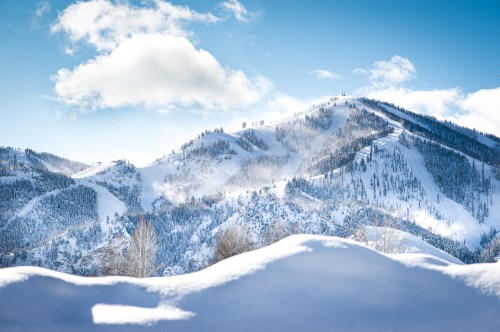 Snow-covered mountains under a blue sky with fluffy clouds, showcasing a serene winter landscape.