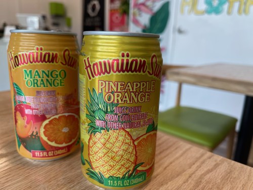Two cans of Hawaiian Sun juice drinks: Mango Orange and Pineapple Orange, displayed on a wooden table.