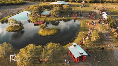 Aerial view of a park with a pond, people enjoying activities, and colorful structures scattered around the landscape.