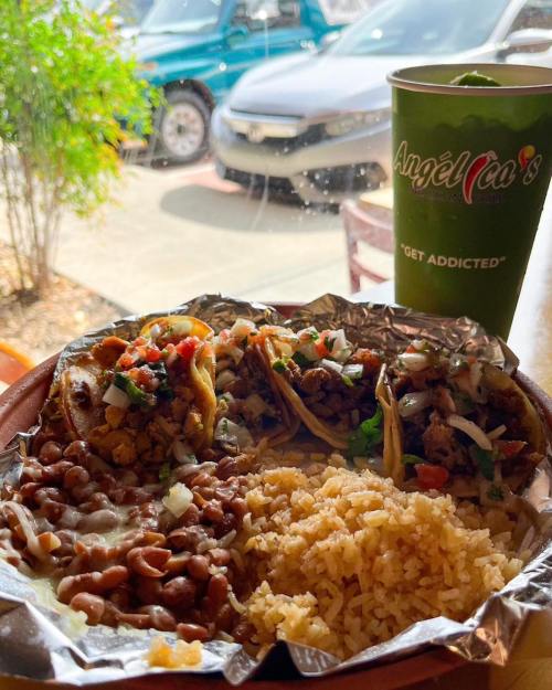 A plate of tacos with rice and beans, alongside a drink, set against a sunny outdoor backdrop.