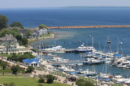A scenic view of a marina with boats, waterfront homes, and a calm blue lake under a clear sky.