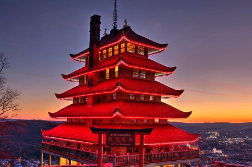 A red pagoda illuminated at sunset, overlooking a city with a clear sky in the background.