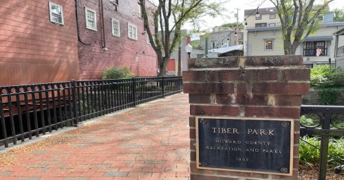 A brick sign for Tiber Park, surrounded by trees and buildings, with a pathway leading through the park.