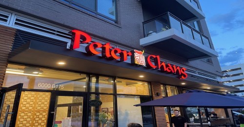 Sign for "Peter Chao's" restaurant illuminated at dusk, with modern architecture and outdoor seating visible.