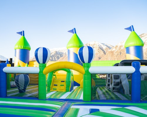 Colorful inflatable bounce house with towers and slides, set against a backdrop of mountains and clear blue sky.