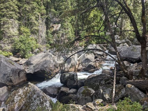 A serene river flows through a rocky landscape, surrounded by lush green trees and boulders.