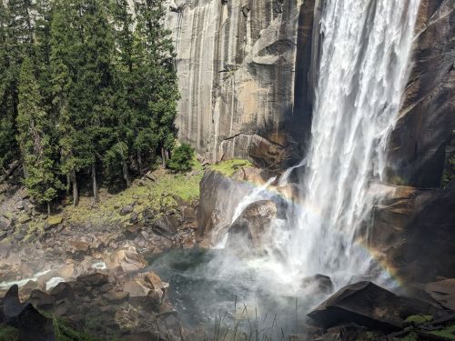 A majestic waterfall cascades over rocky cliffs, creating a misty pool below with a faint rainbow in the spray.