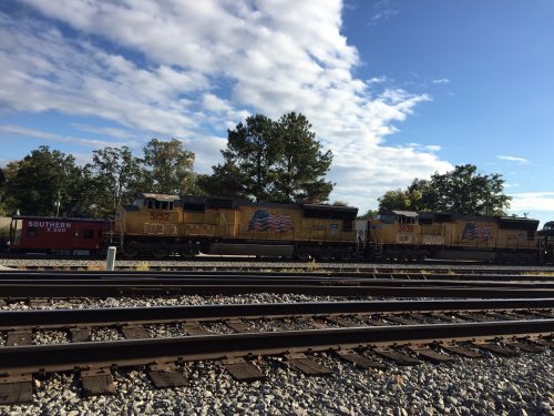 Two yellow locomotives with American flag designs parked on tracks under a blue sky with scattered clouds.
