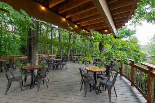 A wooden deck surrounded by trees, featuring several tables and chairs, creating a serene outdoor dining space.