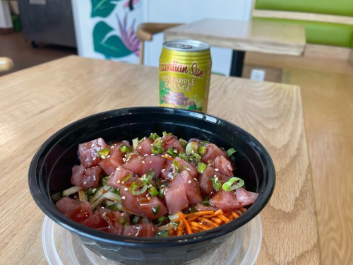 A bowl of poke with diced fish, green onions, and sesame seeds, alongside a can of Hawaiian Sun Pineapple Orange drink.