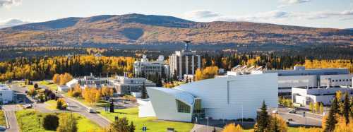 Aerial view of a modern building surrounded by autumn foliage and mountains in the background.