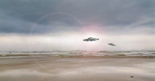 Two UFOs hover above a beach under a cloudy sky, with waves gently lapping at the shore.