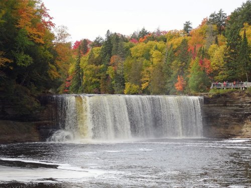 A scenic waterfall surrounded by vibrant autumn foliage and a calm river below.