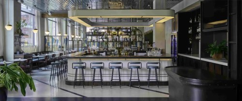 Modern bar area with sleek design, high stools, and a well-stocked shelf behind the counter, featuring large windows.