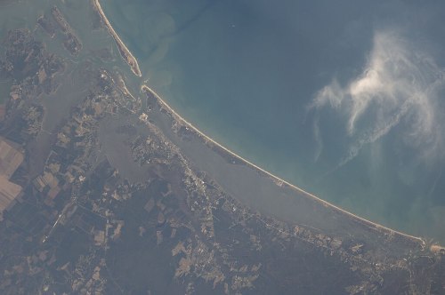 Aerial view of a coastal area with a curved shoreline, surrounded by water and patches of land.