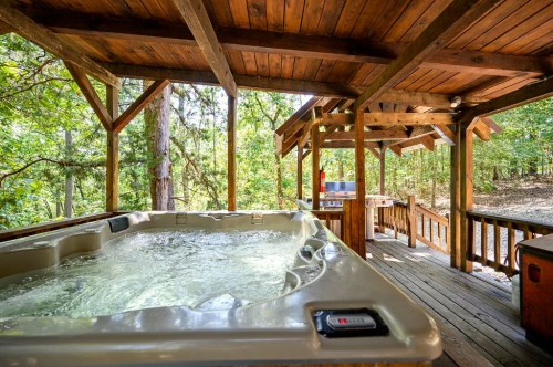 A wooden gazebo with a hot tub and outdoor kitchen, surrounded by trees and nature.