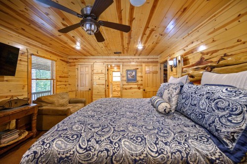 Cozy wooden cabin interior featuring a large bed with blue patterned bedding, a fan, and a comfortable seating area.