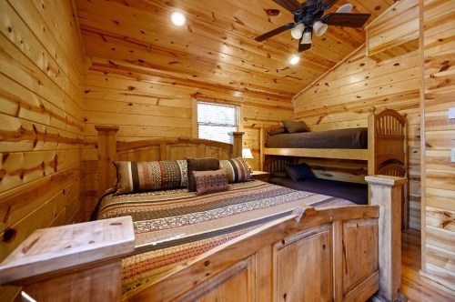 Cozy wooden bedroom featuring a queen bed and a bunk bed, with warm lighting and rustic decor.