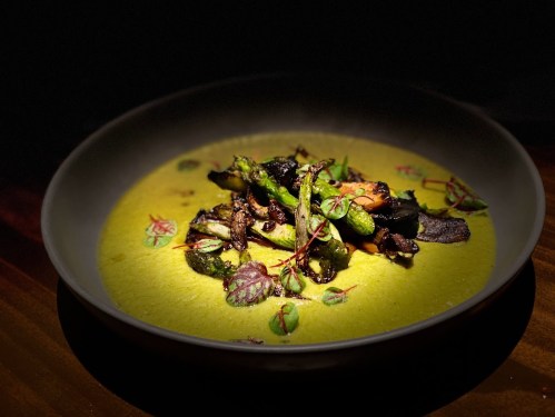 A beautifully plated dish featuring vibrant green vegetables on a creamy yellow sauce, garnished with herbs.