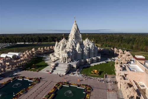 Aerial view of a grand temple surrounded by gardens and fountains, with intricate architecture and lush greenery.