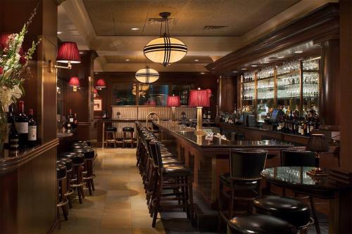 A cozy bar with wooden decor, dim lighting, and a long counter lined with stools and shelves of liquor.