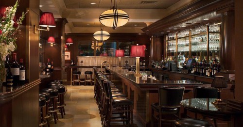Elegant bar interior with wooden accents, dim lighting, and a variety of wine bottles displayed on shelves.