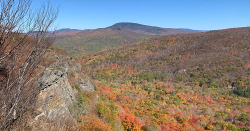 A panoramic view of a colorful autumn landscape with rolling hills and a clear blue sky.