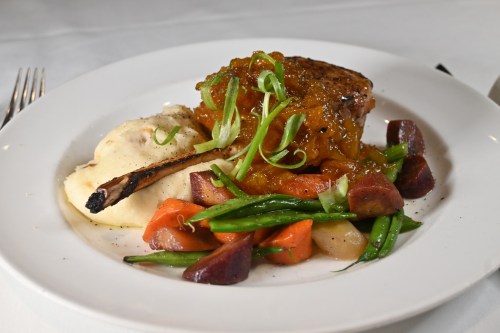 A plated meal featuring grilled meat with sauce, mashed potatoes, and a colorful assortment of vegetables.