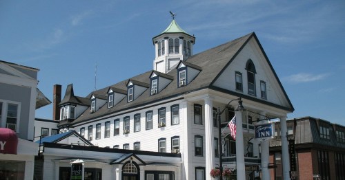 Historic white inn with a green cupola, featuring multiple gabled roofs and a welcoming entrance. Clear blue sky above.