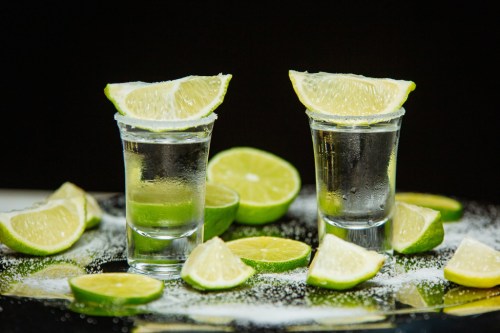 Two shot glasses filled with clear liquid, garnished with lime wedges, surrounded by lime slices and salt.