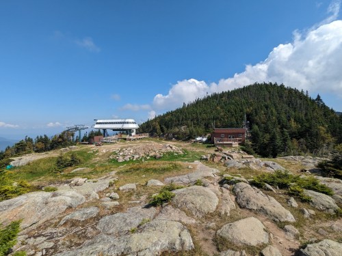 A scenic view of a mountain landscape featuring a ski lift, a lodge, and rocky terrain under a blue sky.
