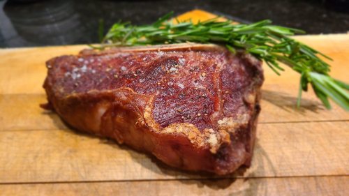 A cooked steak resting on a wooden cutting board, garnished with fresh rosemary.