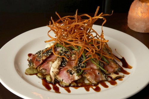 A plate of seared tuna topped with crispy sweet potato strands and drizzled with a dark sauce.