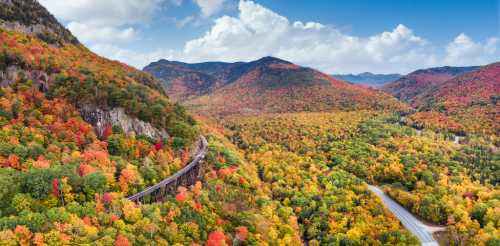 A scenic view of vibrant autumn foliage covering rolling hills and a winding railway through a colorful landscape.