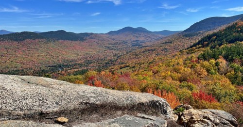 A panoramic view of a colorful autumn landscape with rolling hills and vibrant foliage under a clear blue sky.
