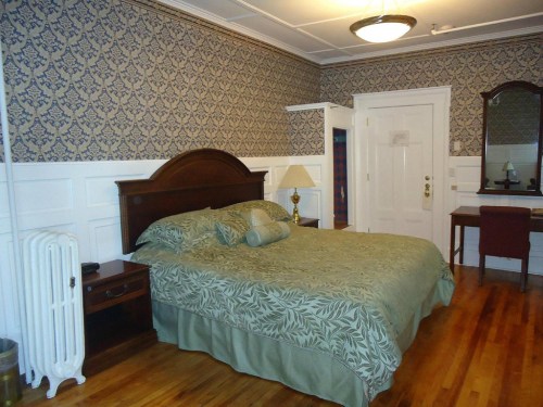 Cozy bedroom with a patterned wallpaper, a large bed, wooden furniture, and a mirror. Warm, inviting atmosphere.