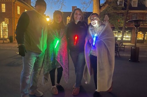 A group of four people in cozy attire, holding colorful light sticks, standing outdoors at night.
