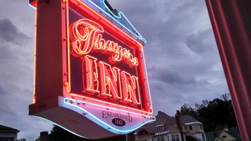 Neon sign for Thayer's Inn, established 1843, against a cloudy sky.