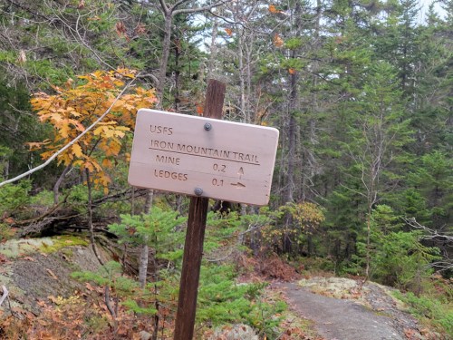 A wooden trail sign for Iron Mountain Trail, indicating distances to Mine (0.2 miles) and Ledges (0.1 miles).
