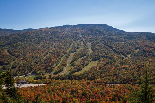 A scenic view of a mountain landscape with vibrant autumn foliage and ski trails winding down the slopes.