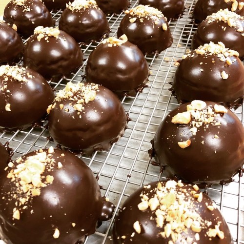 A close-up of chocolate-covered treats topped with crushed nuts, arranged on a cooling rack.