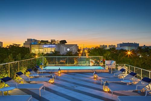 Rooftop pool area at sunset, featuring lounge chairs and lanterns, with city skyline in the background.