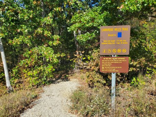 A trail sign for Labarque Hills Trail, surrounded by trees and foliage, indicating trail details and rules.