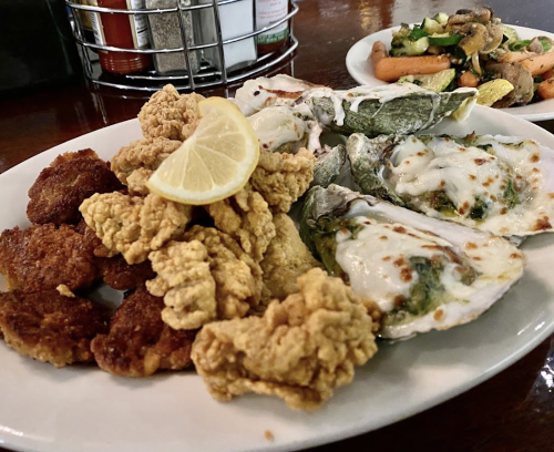 A plate of fried seafood, including crispy oysters and golden-brown fish bites, garnished with a lemon slice.
